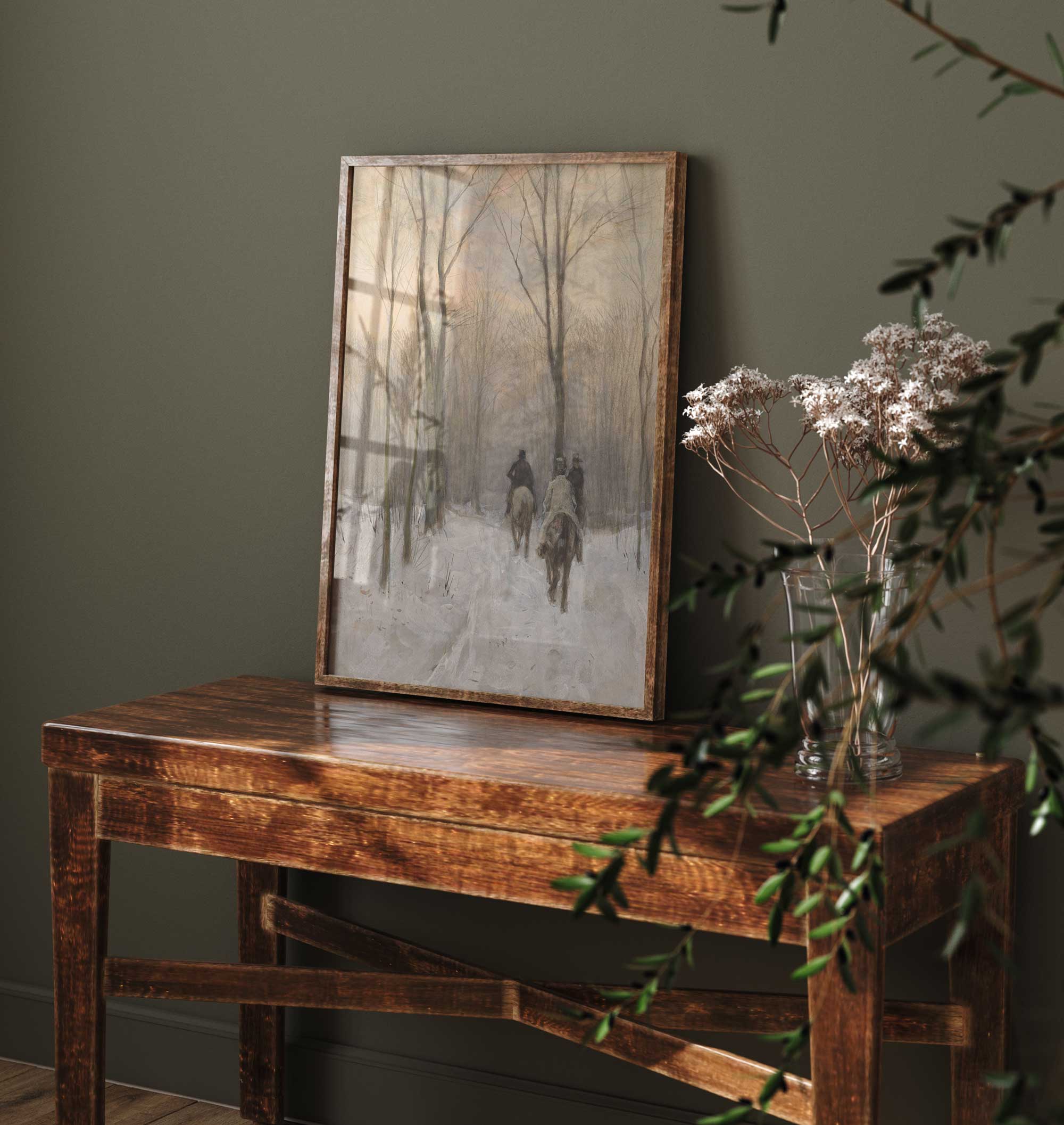 Wooden table with a framed artwork and a vase against a dark green wall.