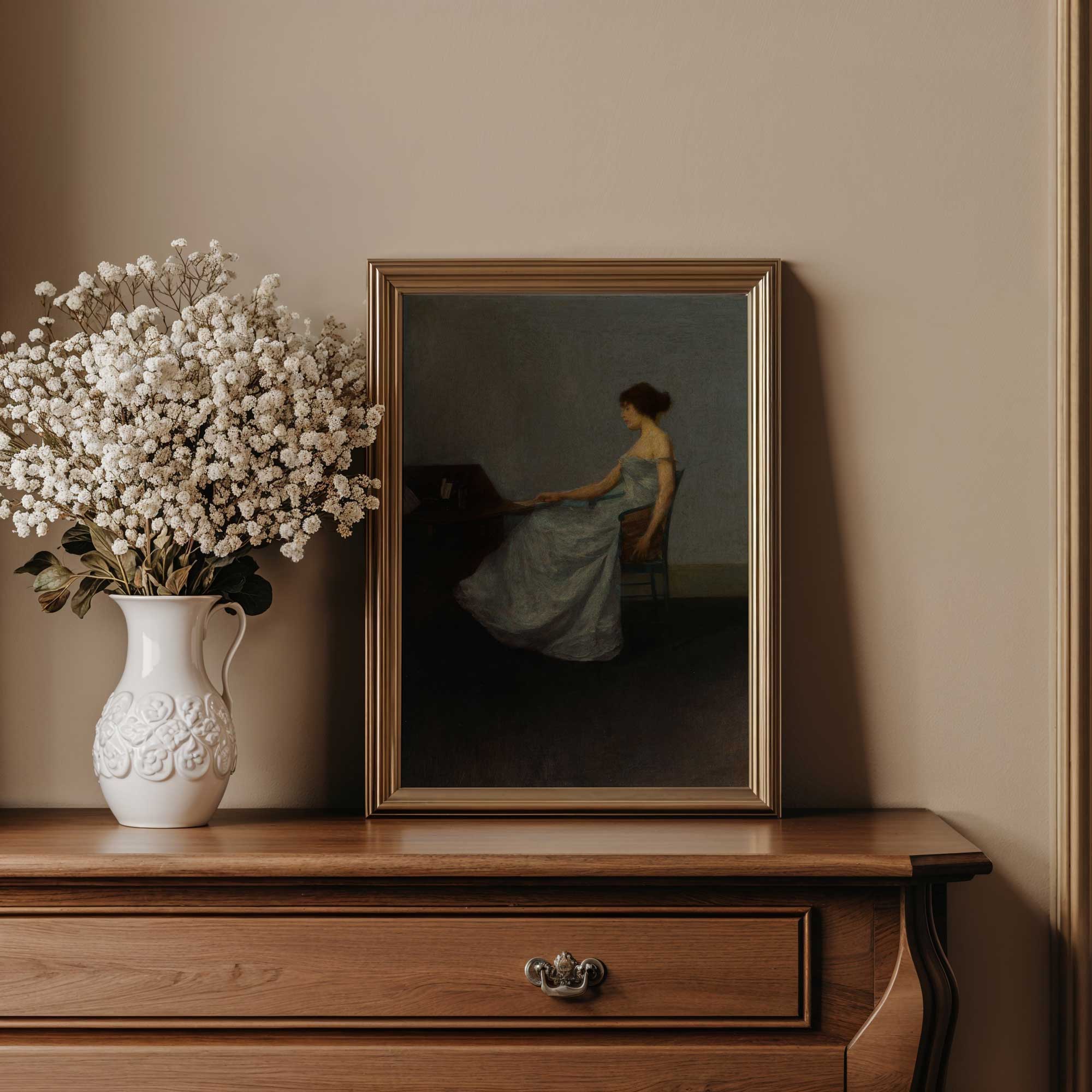 Framed artwork on a wooden dresser with a vase of white flowers.
