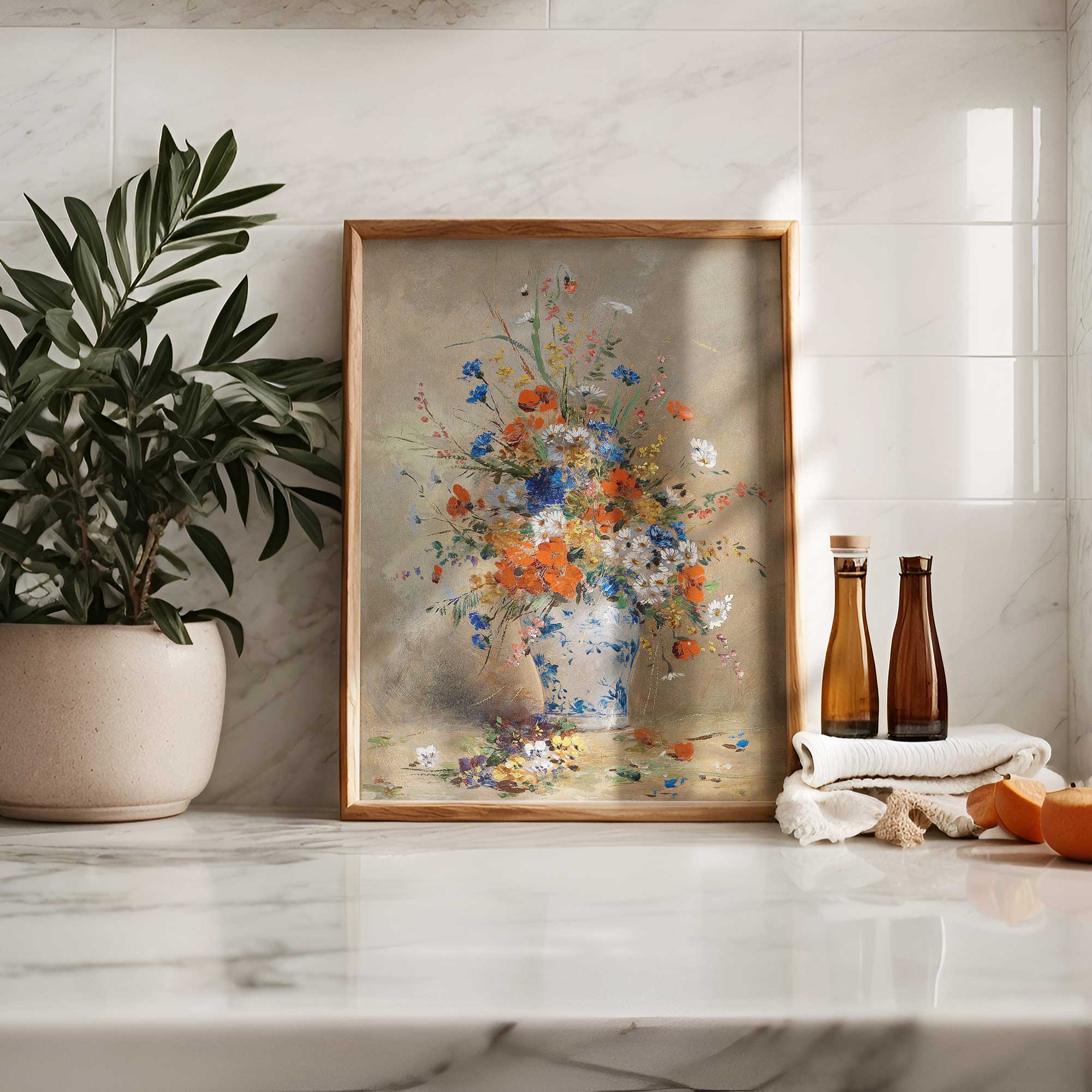 Framed floral painting on a marble surface with a plant and bottles in the background