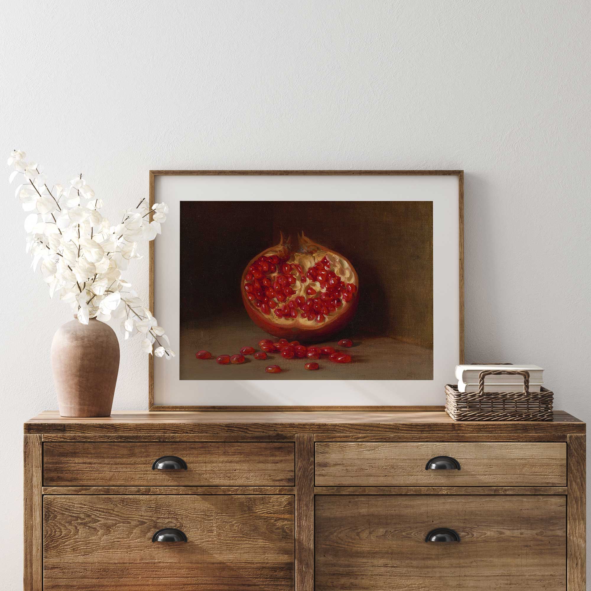 Framed artwork of a pomegranate on a wooden dresser with decorative items.