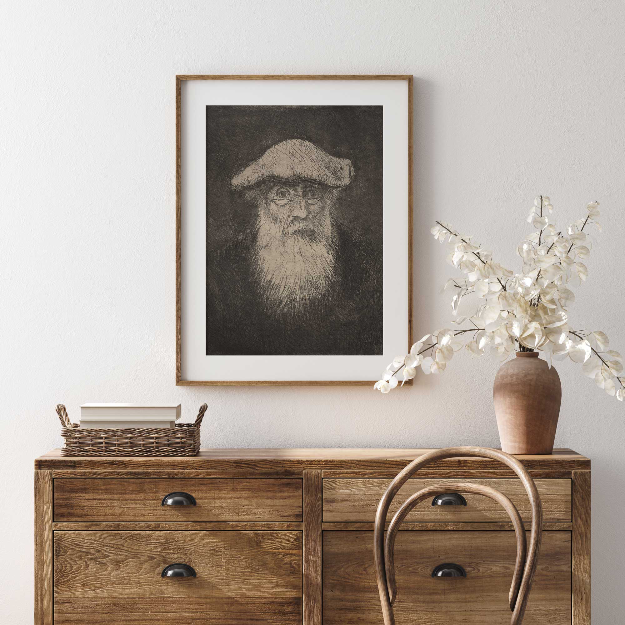 Framed portrait of Camille Pissarro above a wooden dresser with decorative items.