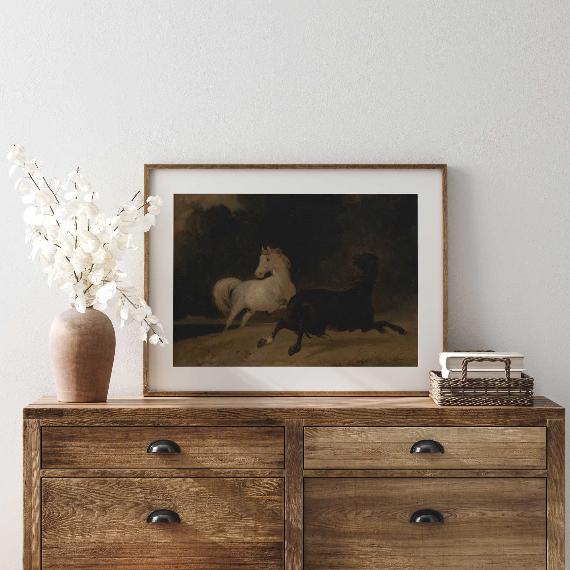 Framed artwork of two horses painting on a wooden dresser with decorative items.