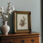 Framed artwork of Vintage Botanical Bird Print next to a vase with flowers on a wooden surface.