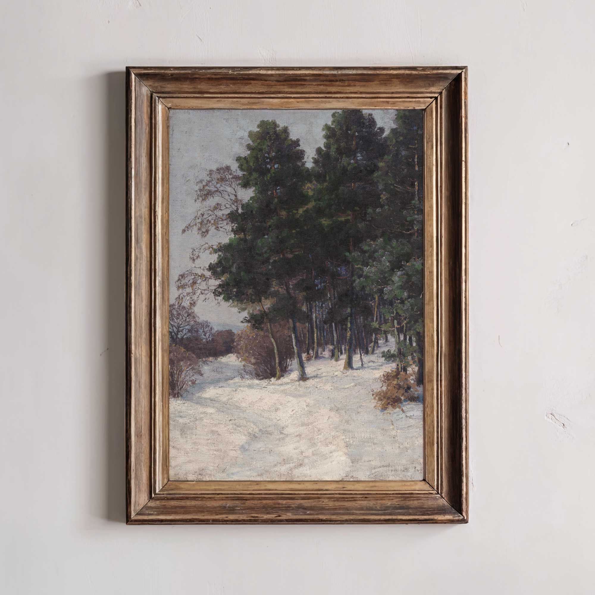 Framed painting of a snowy landscape with trees on a white wall