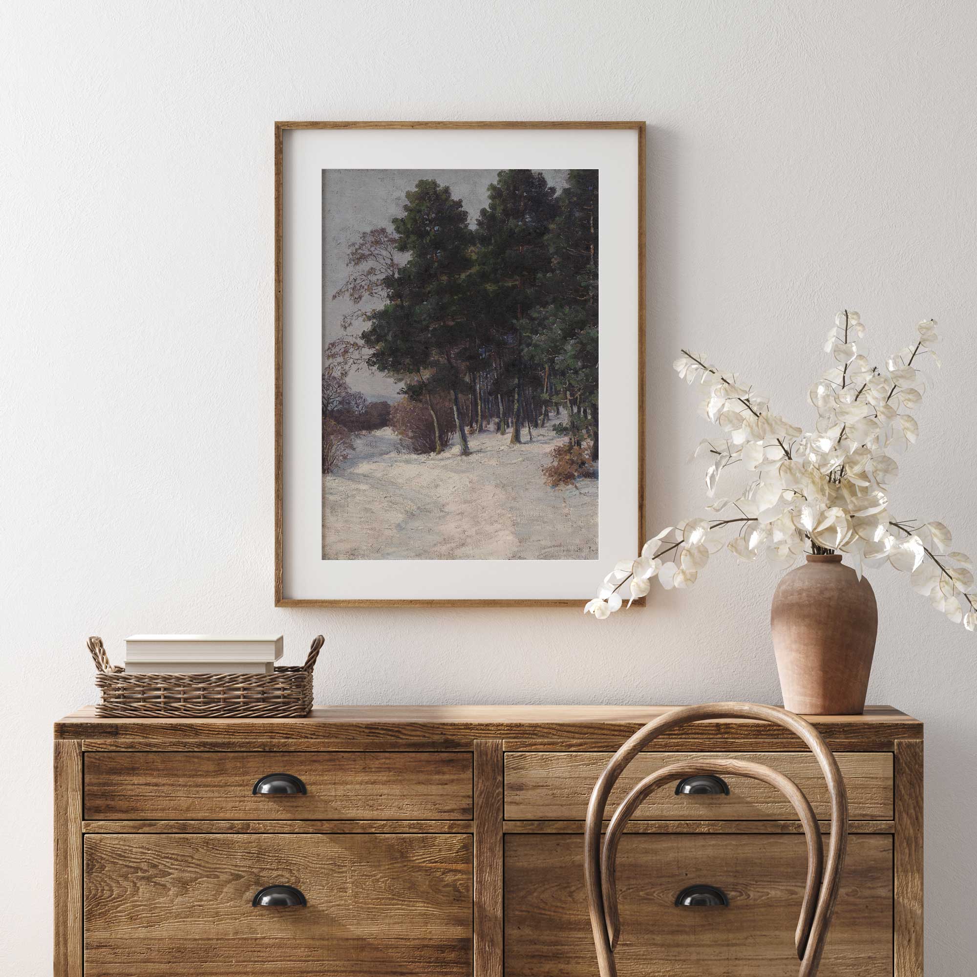 Wooden dresser with framed artwork, basket, and vase on a white wall.