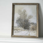 Framed painting of a snowy landscape with trees on a white wall.