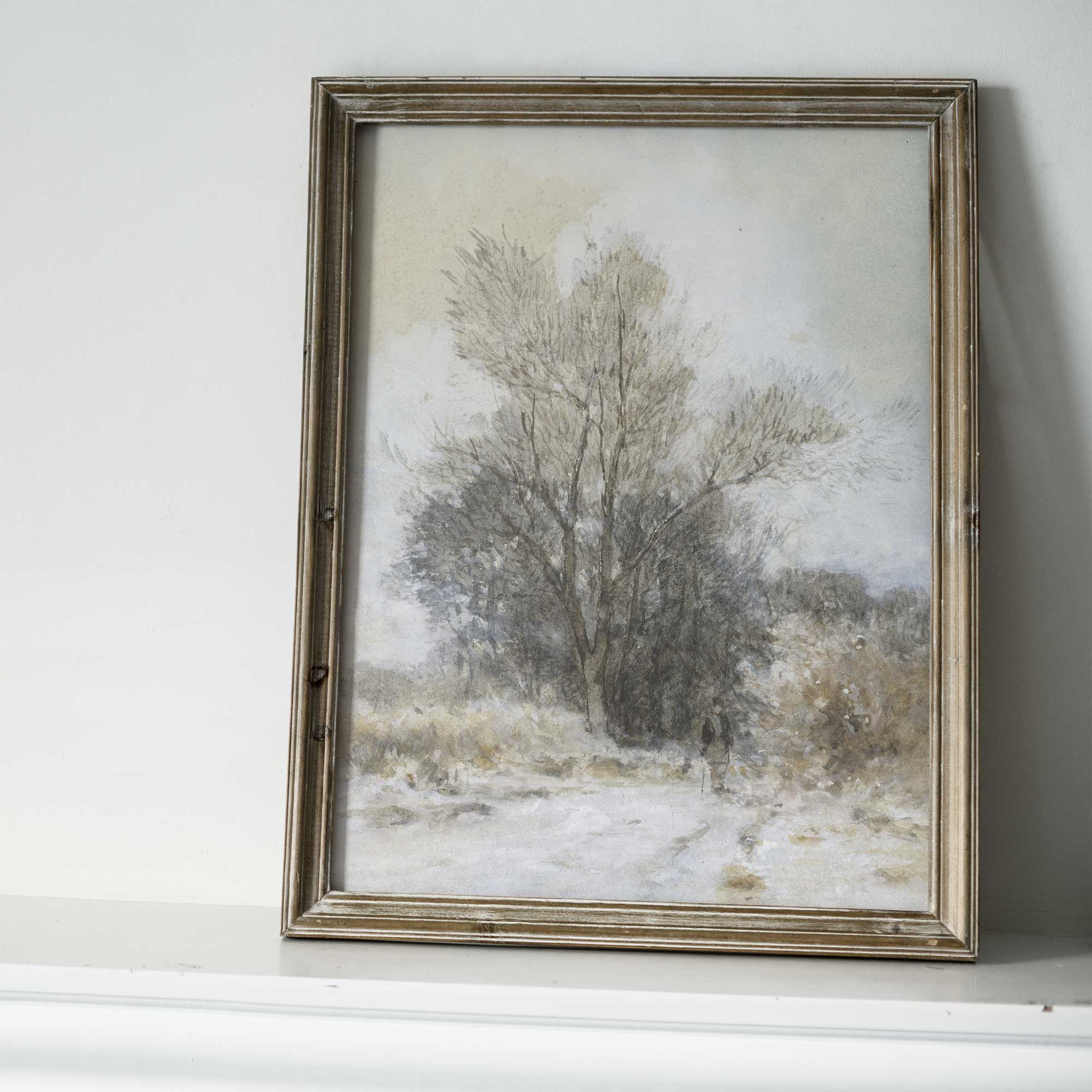 Framed painting of a snowy landscape with trees on a white wall.