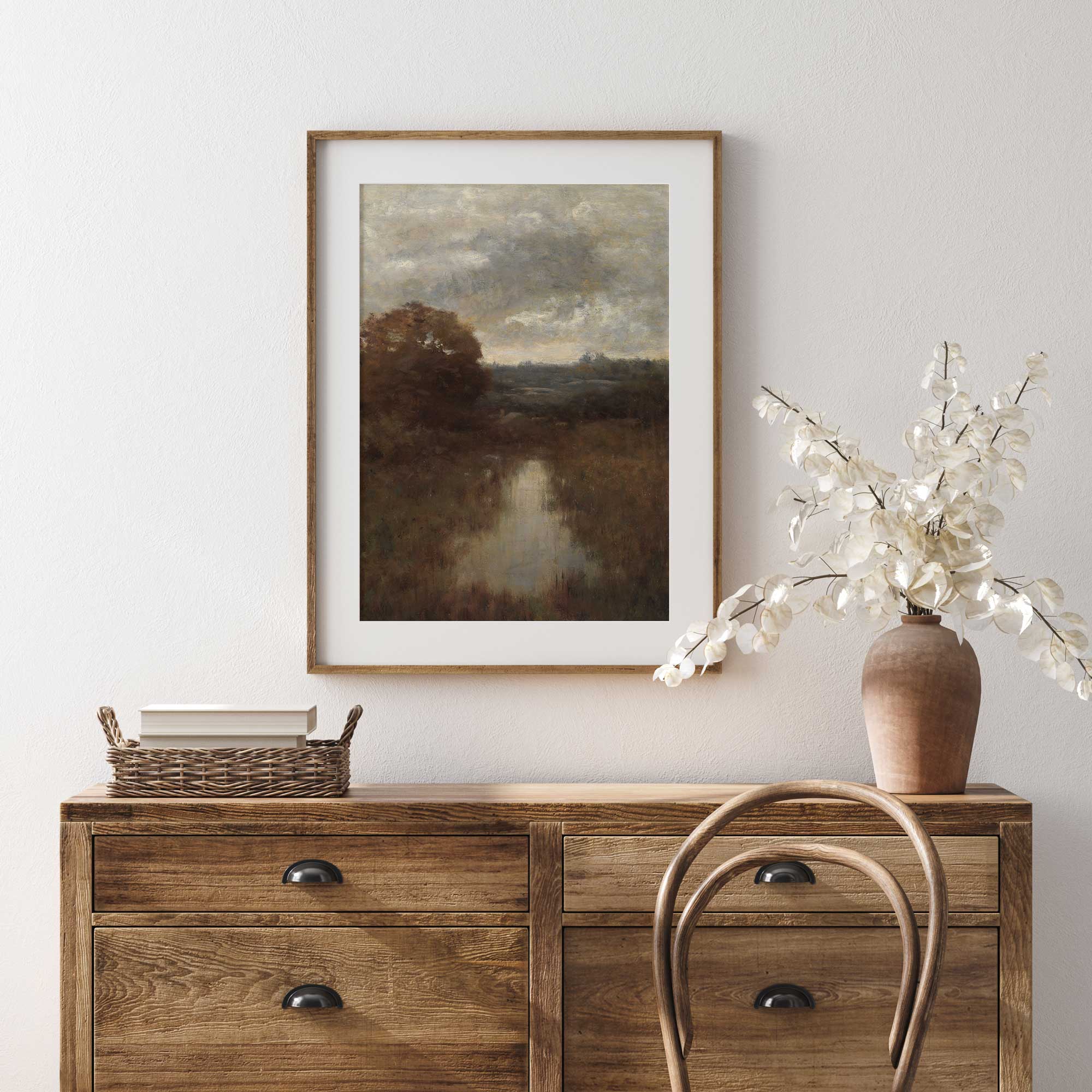 Wooden dresser with a framed Rustic landscape painting Print and decorative items against a light wall.