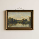 Framed French landscape painting of a river scene with trees on a white wall.