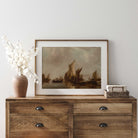 Wooden dresser with a framed painting, vase, and stack of books against a white wall.