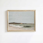 Framed artwork of a vintage coastal scene with a beach and ocean on a white wall.