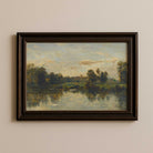 Framed painting of a landscape with a river and trees on a beige wall.