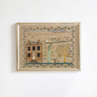 Whimsical folk art house print in light gold frame on a white wall