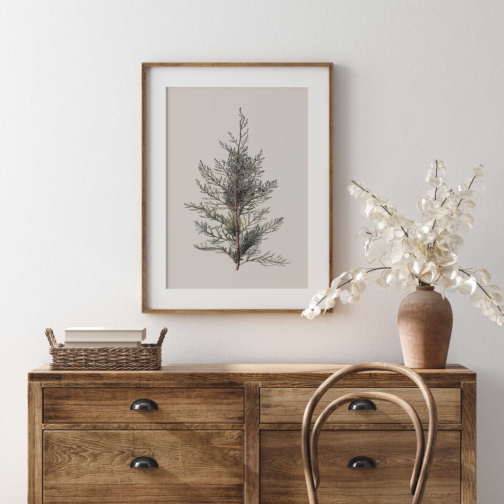 Wooden dresser with framed  juniper branch vintage botanical print and decorative items against a white wall