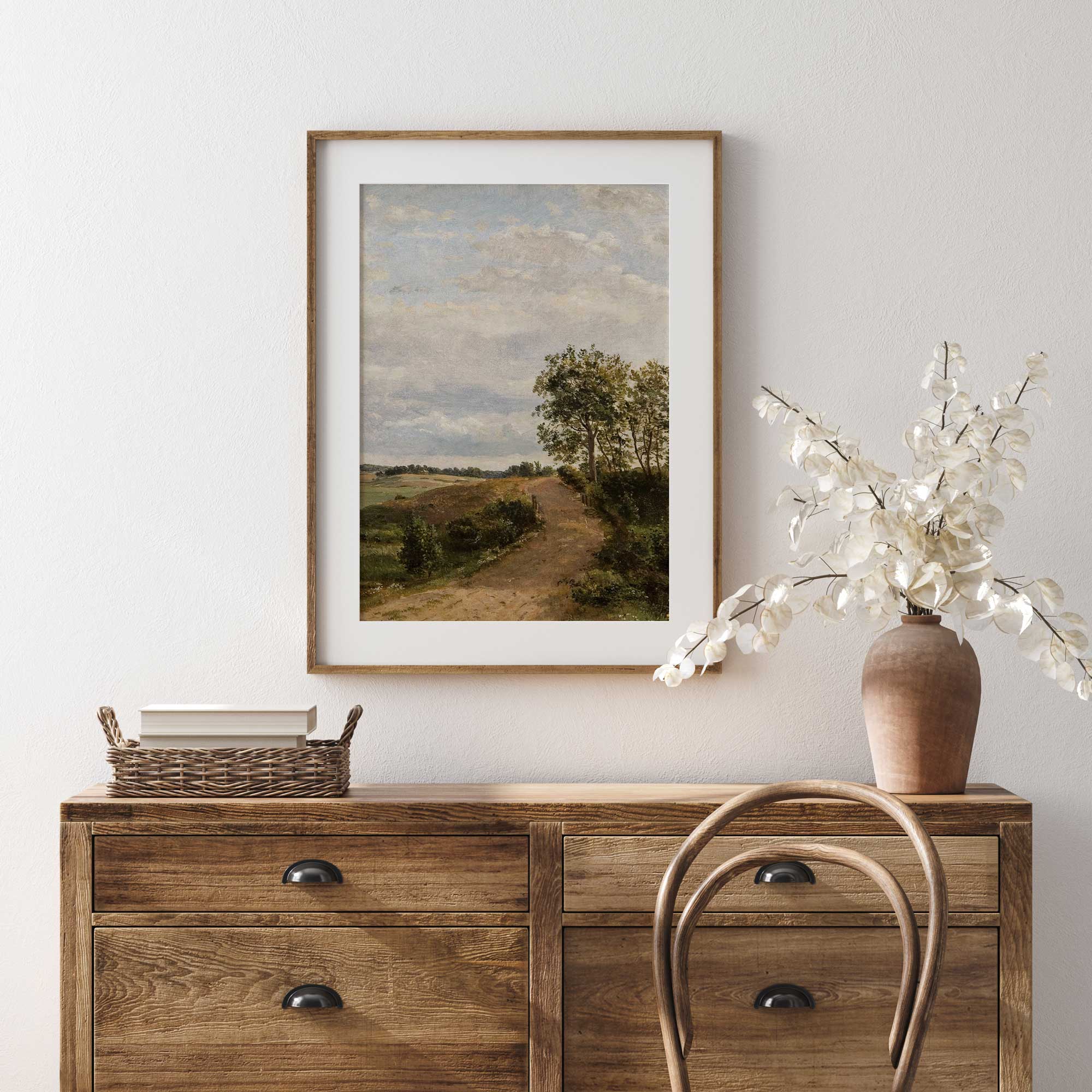 Wooden dresser with The Country Road vintage landscape print in oak frame  and decorative items against a light wall.