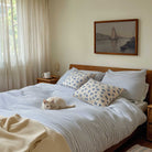 Cat lying on a bed with striped bedding and decorative pillows, with a sailboat  painting on the wall.