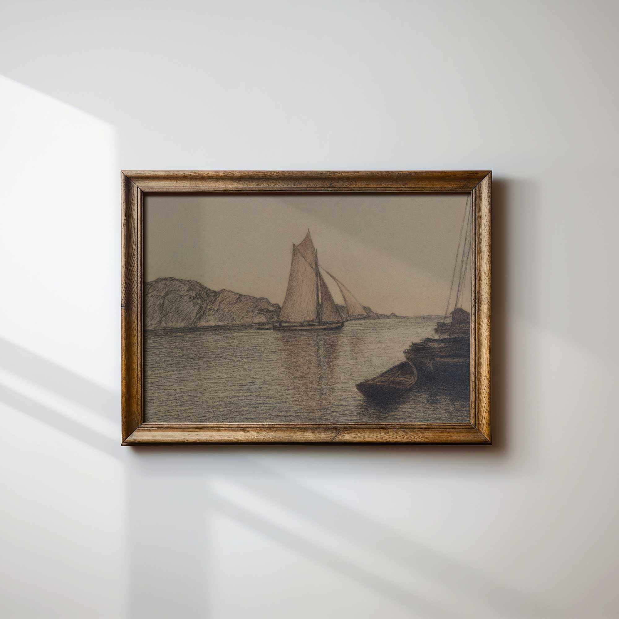 Framed artwork of a sailboat on water with mountains, on a white wall.