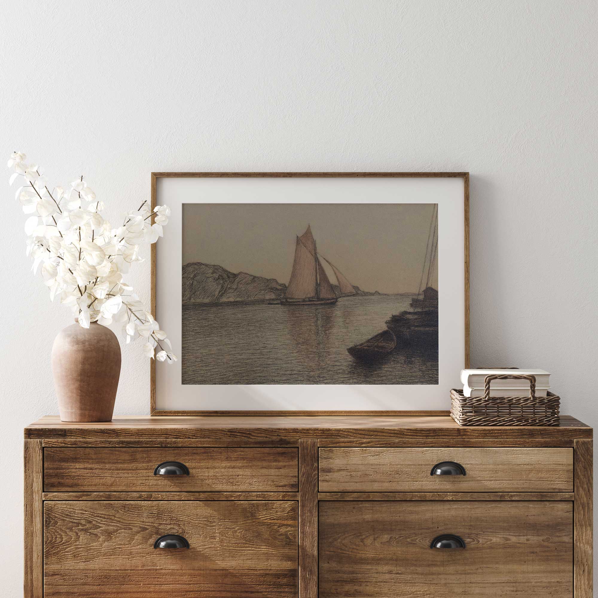 Wooden dresser with framed sail boat artwork, vase, and basket against a white wall