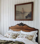 Bedroom with wooden headboard, floral pillows, and framed artwork of sailboats.