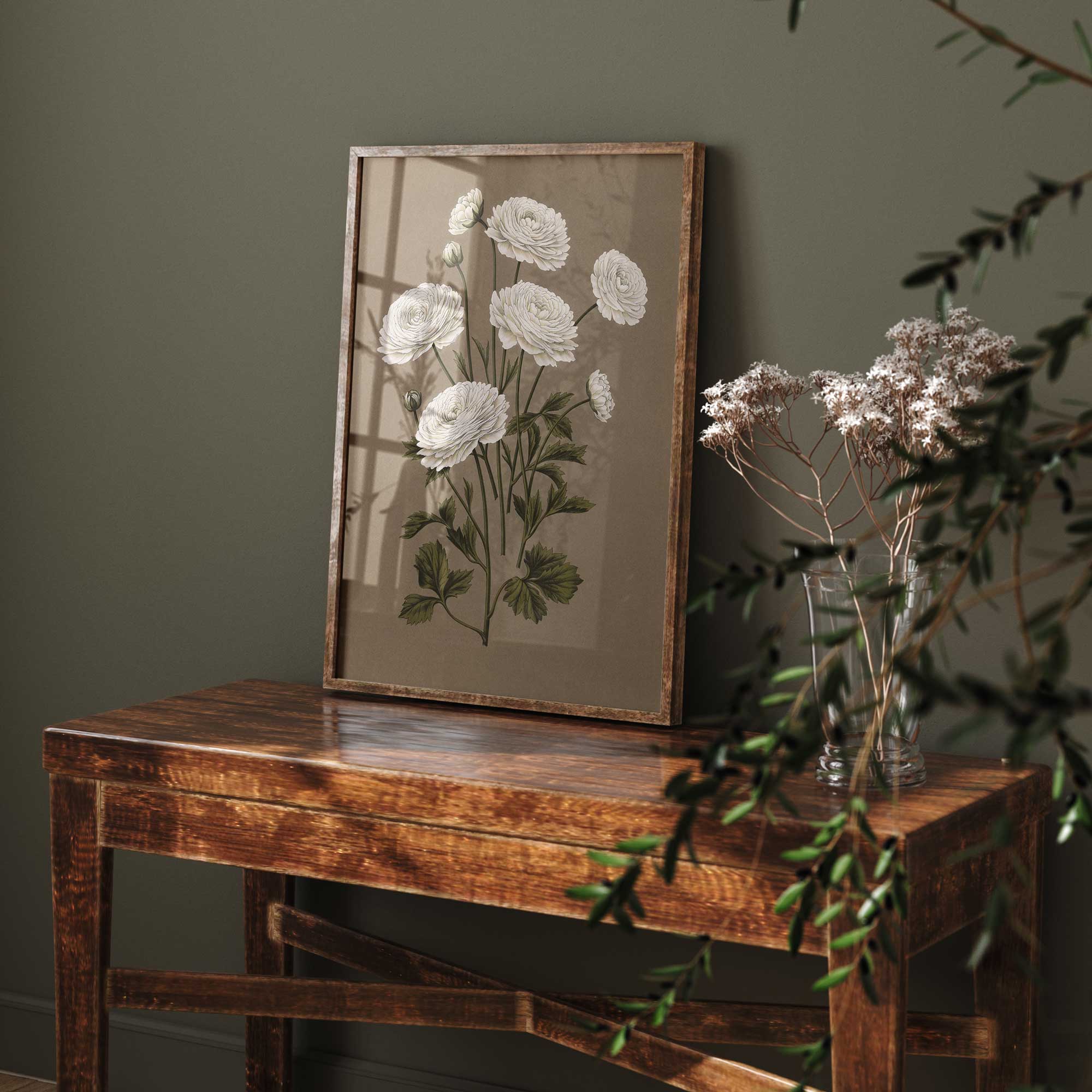 Framed botanical print of white flowers on a wooden table against a dark green wall.