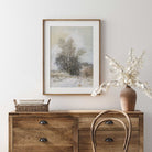 Wooden dresser with a framed landscape painting and decorative items against a white wall.