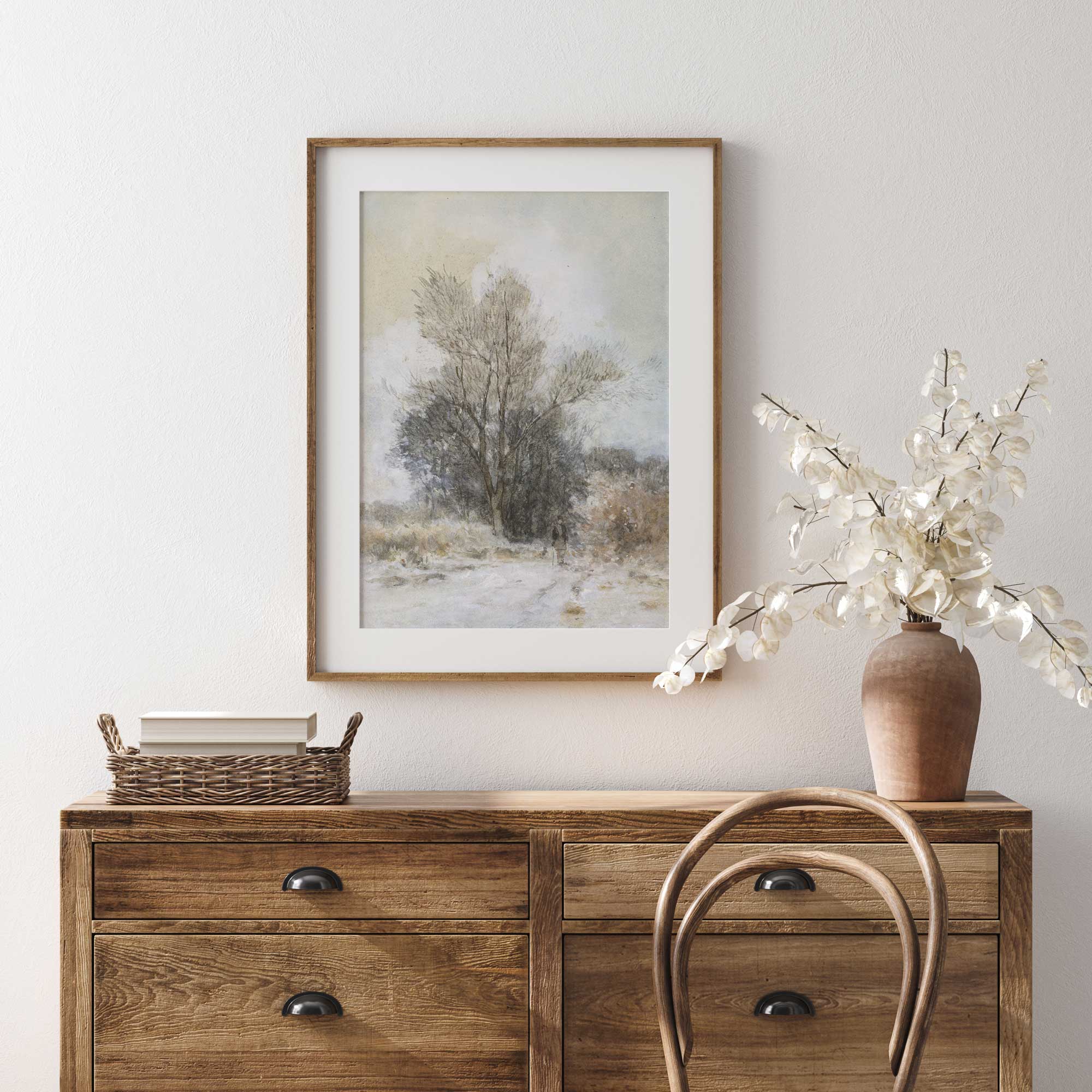 Wooden dresser with a framed landscape painting and decorative items against a white wall.